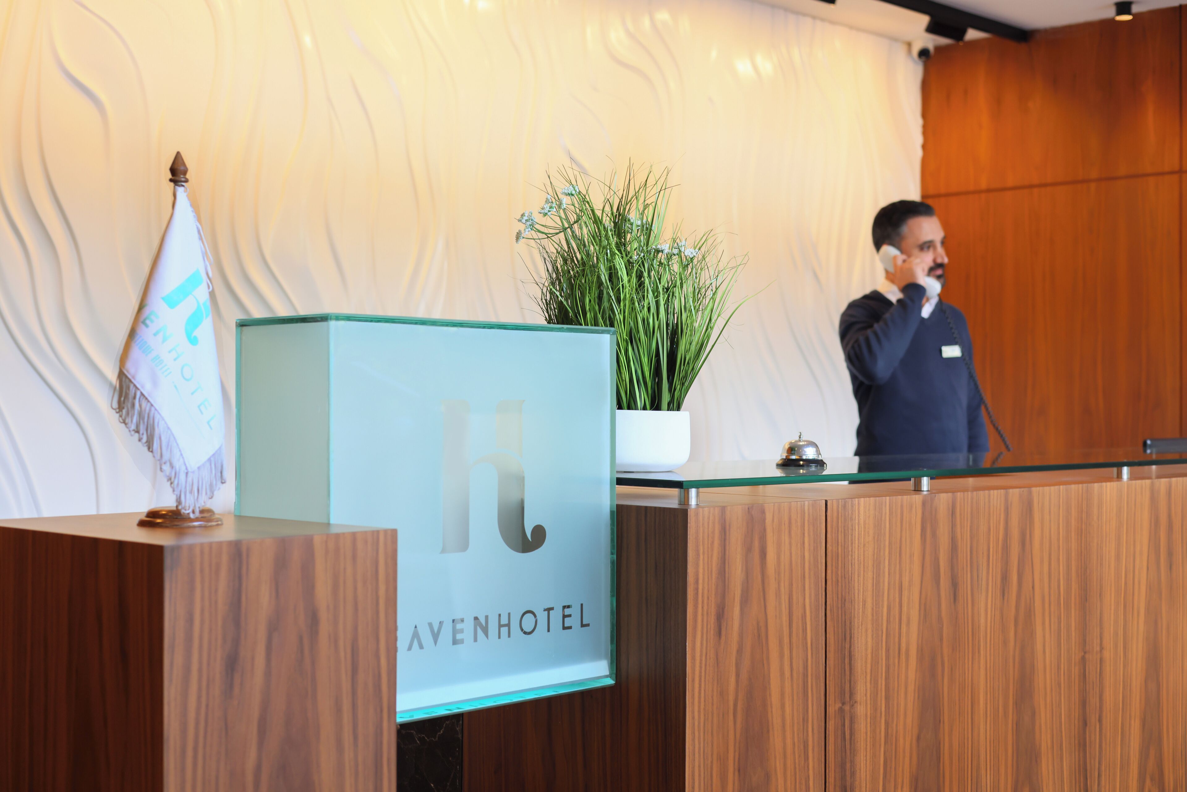 Uma receção de hotel com acabamento em madeira, uma vitrine de vidro e uma planta em vaso.