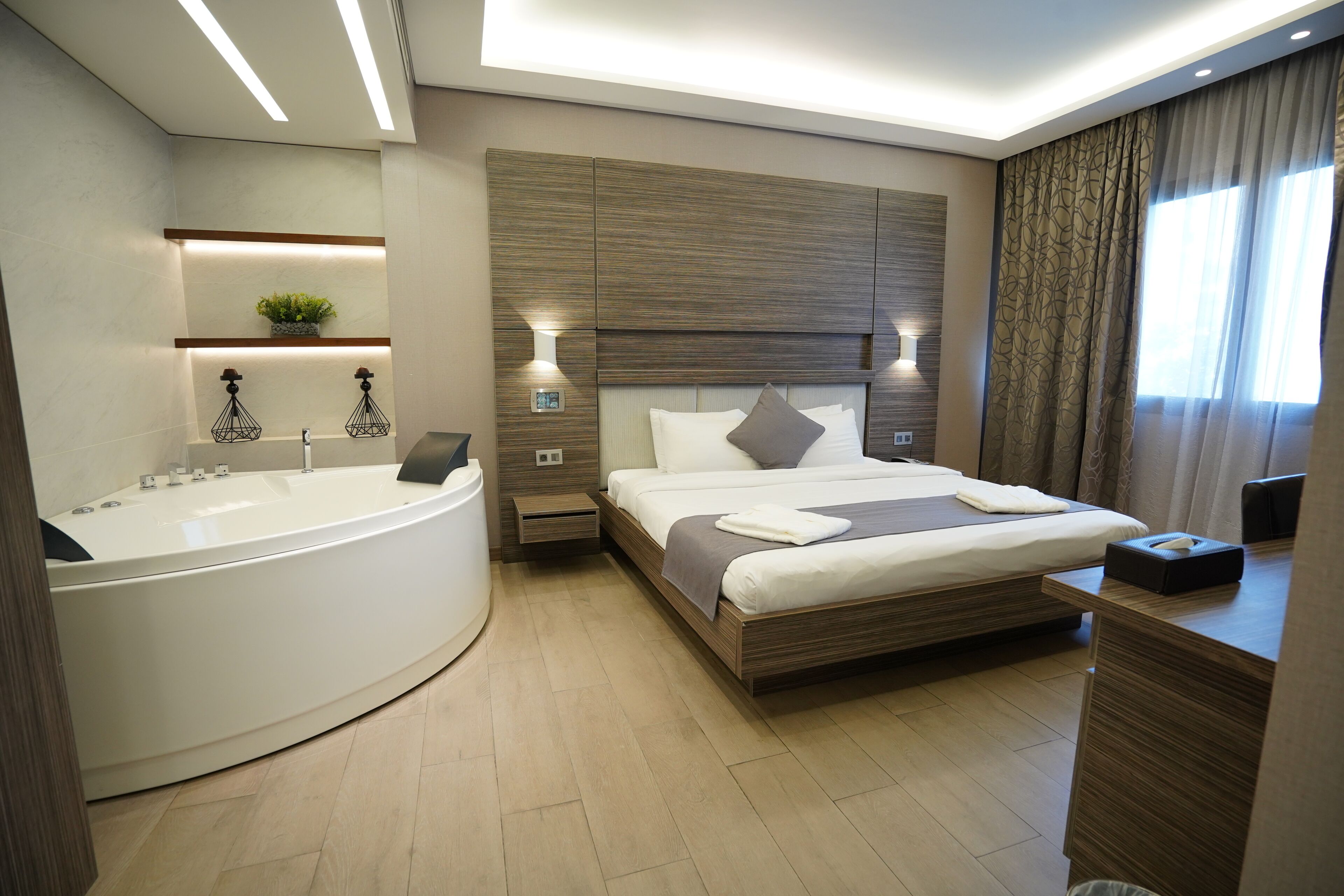Una habitación de hotel moderna con una cama grande, un baño separado con bañera y una mesita de noche con lámpara.