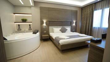 Una habitación de hotel moderna con una cama grande, un baño separado con bañera y una mesita de noche con lámpara.