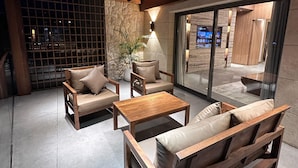 A modern interior with a wooden ceiling, a stone wall, and a glass door leading outside. There are wooden furniture pieces including a sofa, chairs, and a coffee table. - Heaven Prestige Hotel (Kfar Yassine)