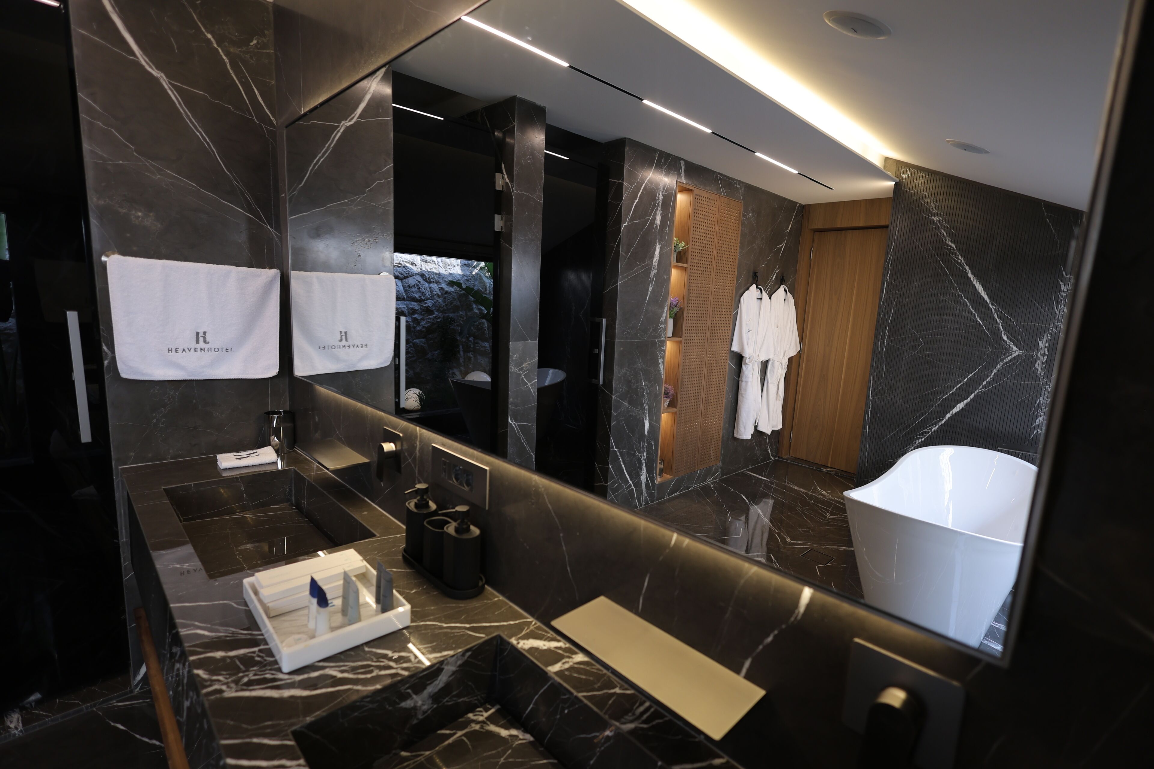 A modern bathroom with a large mirror, marble walls, and a bathtub.