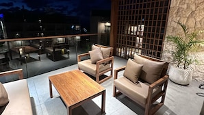 A modern outdoor seating area with wooden furniture and a stone wall backdrop. - Heaven Prestige Hotel (Kfar Yassine)