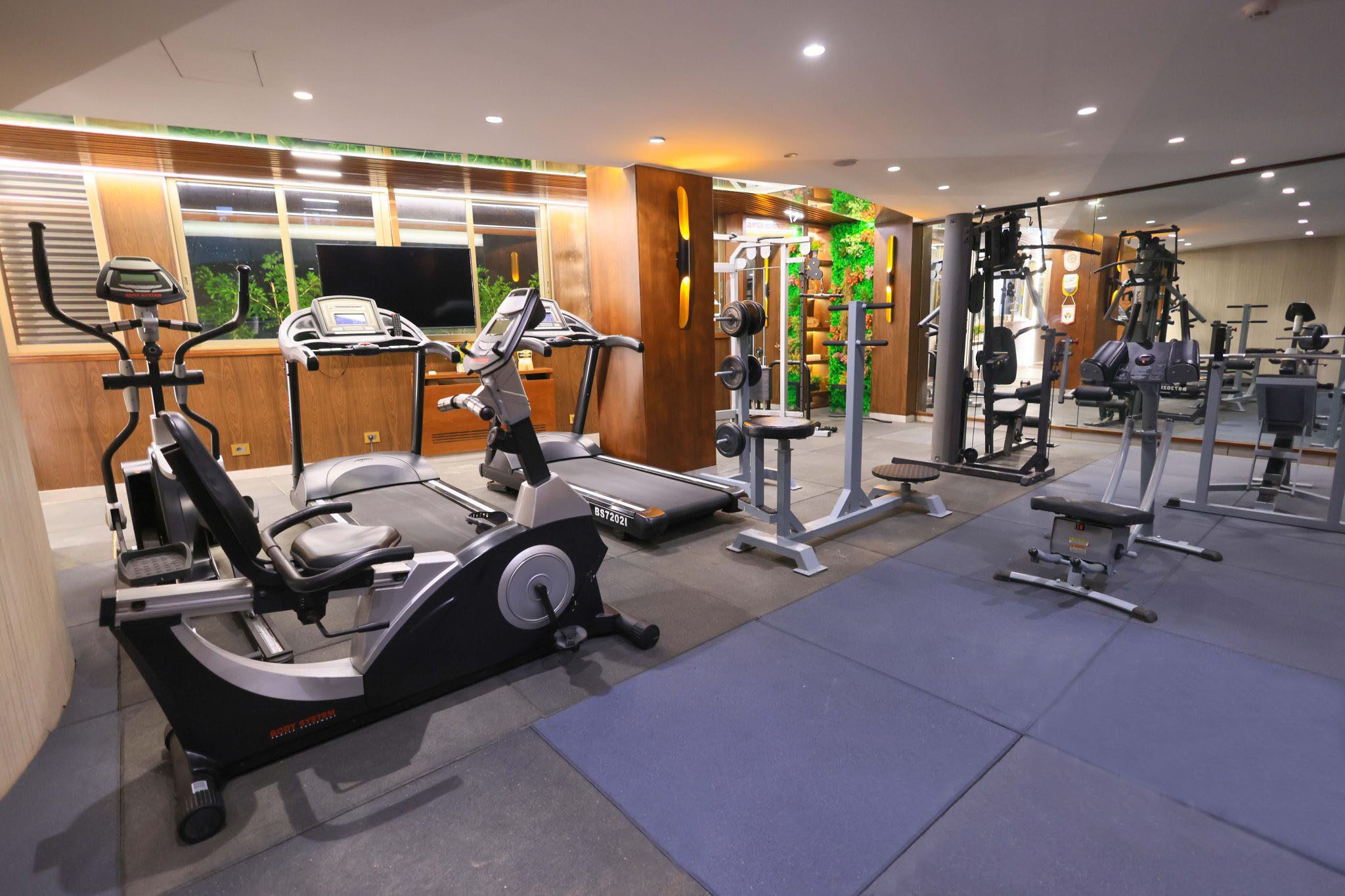 Un gimnasio con diversos equipos de ejercicio, incluyendo cintas de correr, una elíptica y máquinas de pesas.