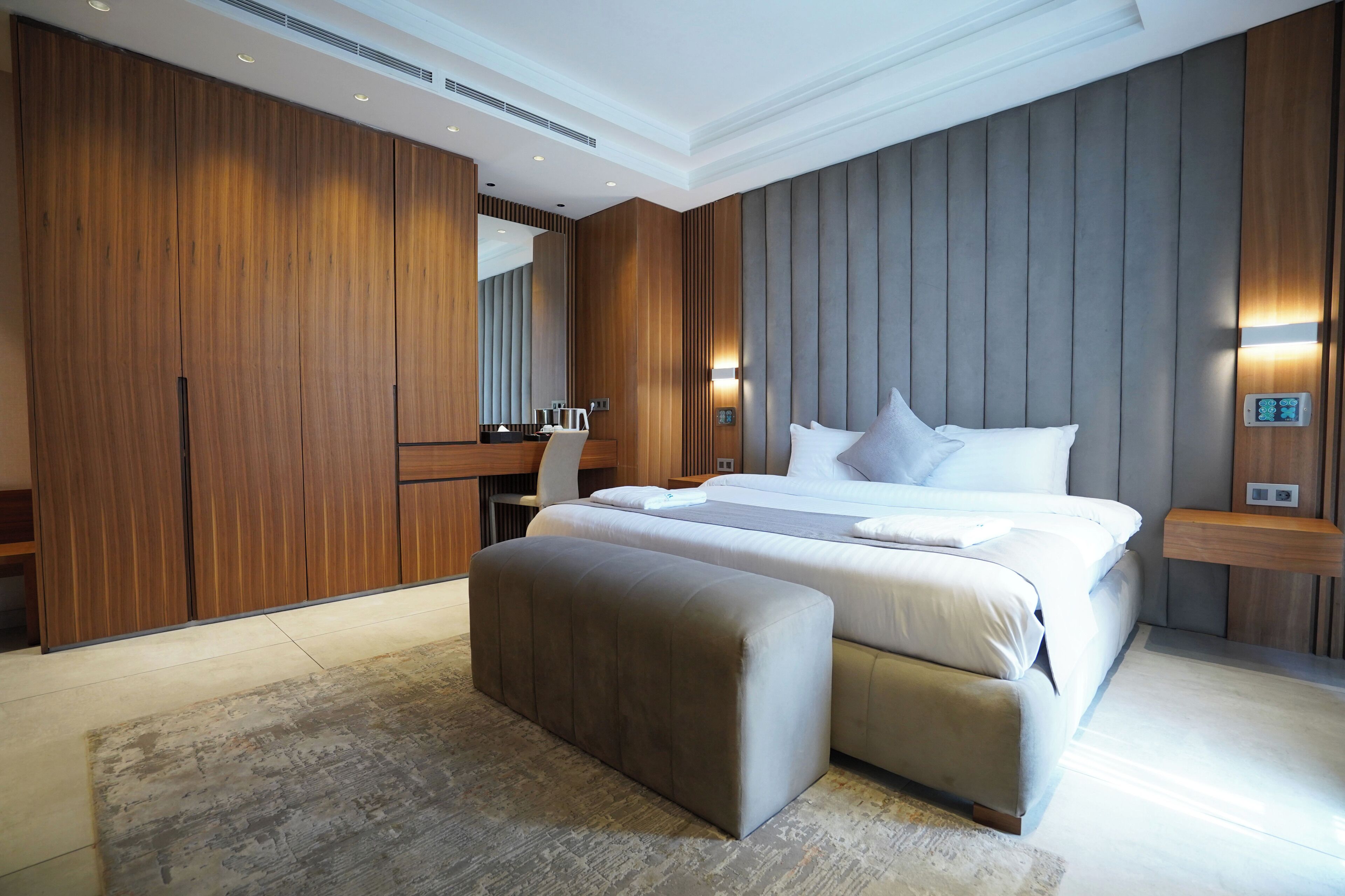 A modern bedroom with a large bed, a wooden wardrobe, a desk, and a bench.