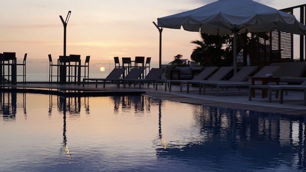 A serene pool area with lounge chairs and umbrellas, overlooking a calm body of water and a sunset. - Heaven Prestige Hotel (Kfar Yassine)