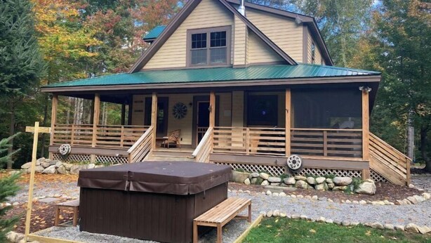 Una casa de dues plantes amb un porxo cobert, una banyera hidromassatge i una llar de pedra.
