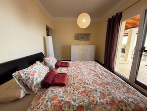 Una habitación de hotel con cama, armario, lámpara colgante y vistas a través de un ventanal.