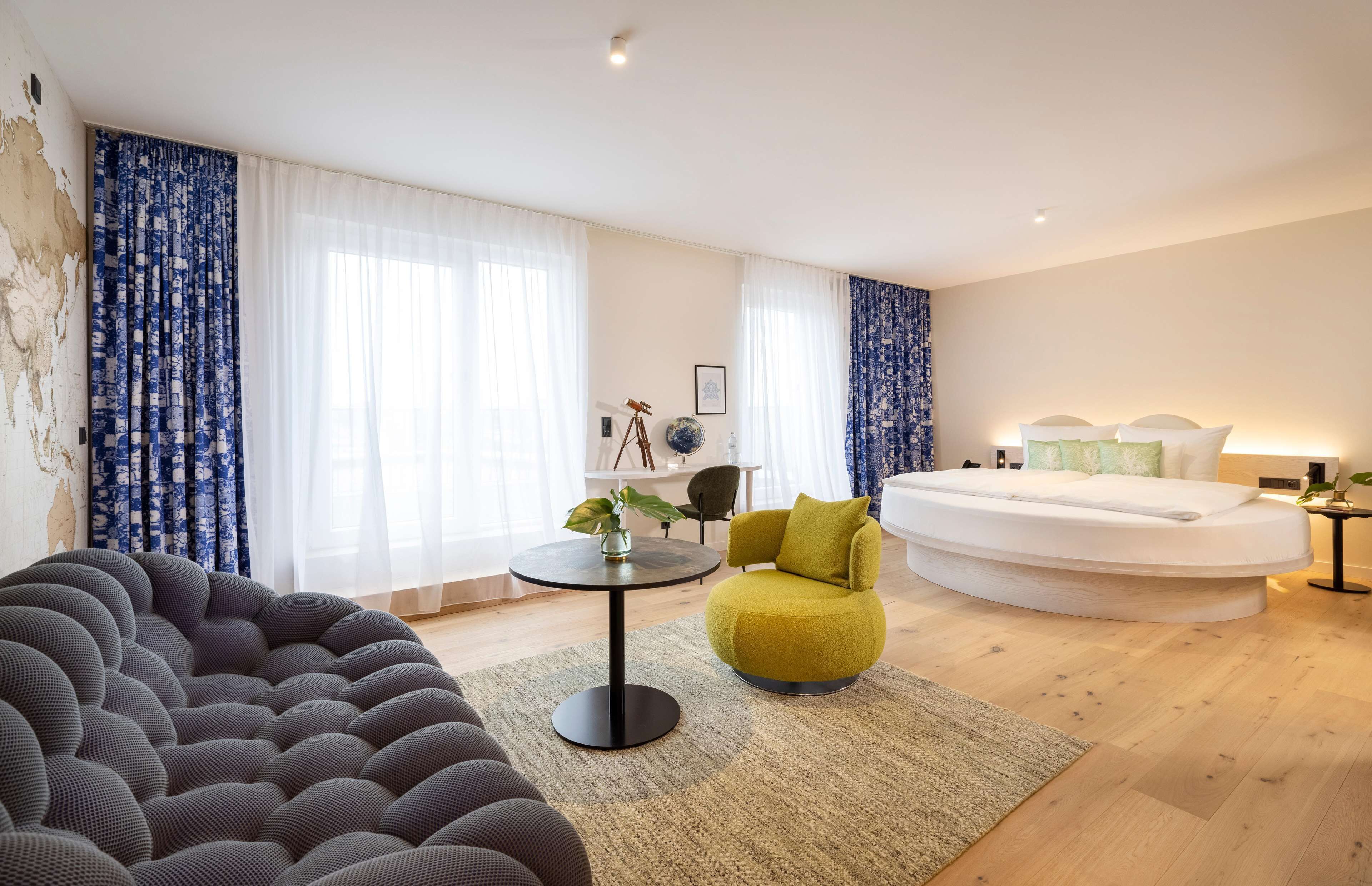 Et moderne hotelværelse med en rund seng, en sofa, et lille bord med en plante og en stol.