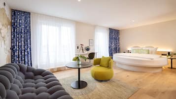 Een moderne hotelkamer met een rond bed, een slaapbank, een bijzettafeltje met een plant en een stoel.