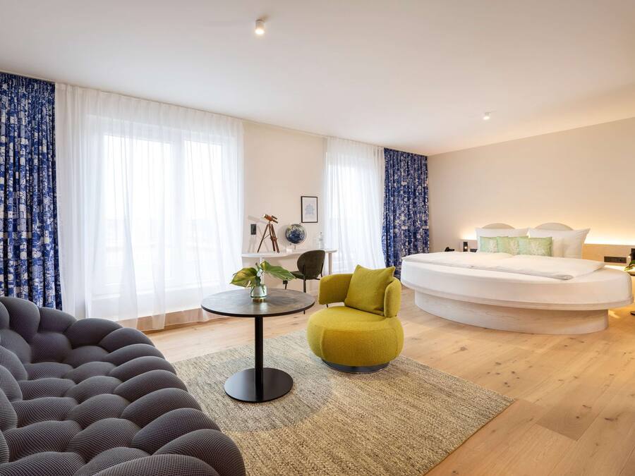 Een moderne hotelkamer met een rond bed, een slaapbank, een bijzettafeltje met een plant en een stoel.