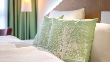 A bed with white bedding and green pillows with white tree patterns.