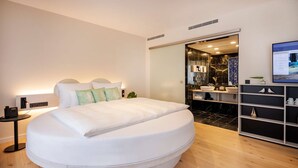 A modern bedroom with a large bed, a bedside table with a phone, and a bathroom visible through a sliding door. - ARCOTEL HafenCity Dresden (Dresden)