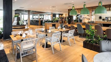 Ein modernes Restaurant mit Holztischen und -stühlen, einer Bar und grünen Pendelleuchten.