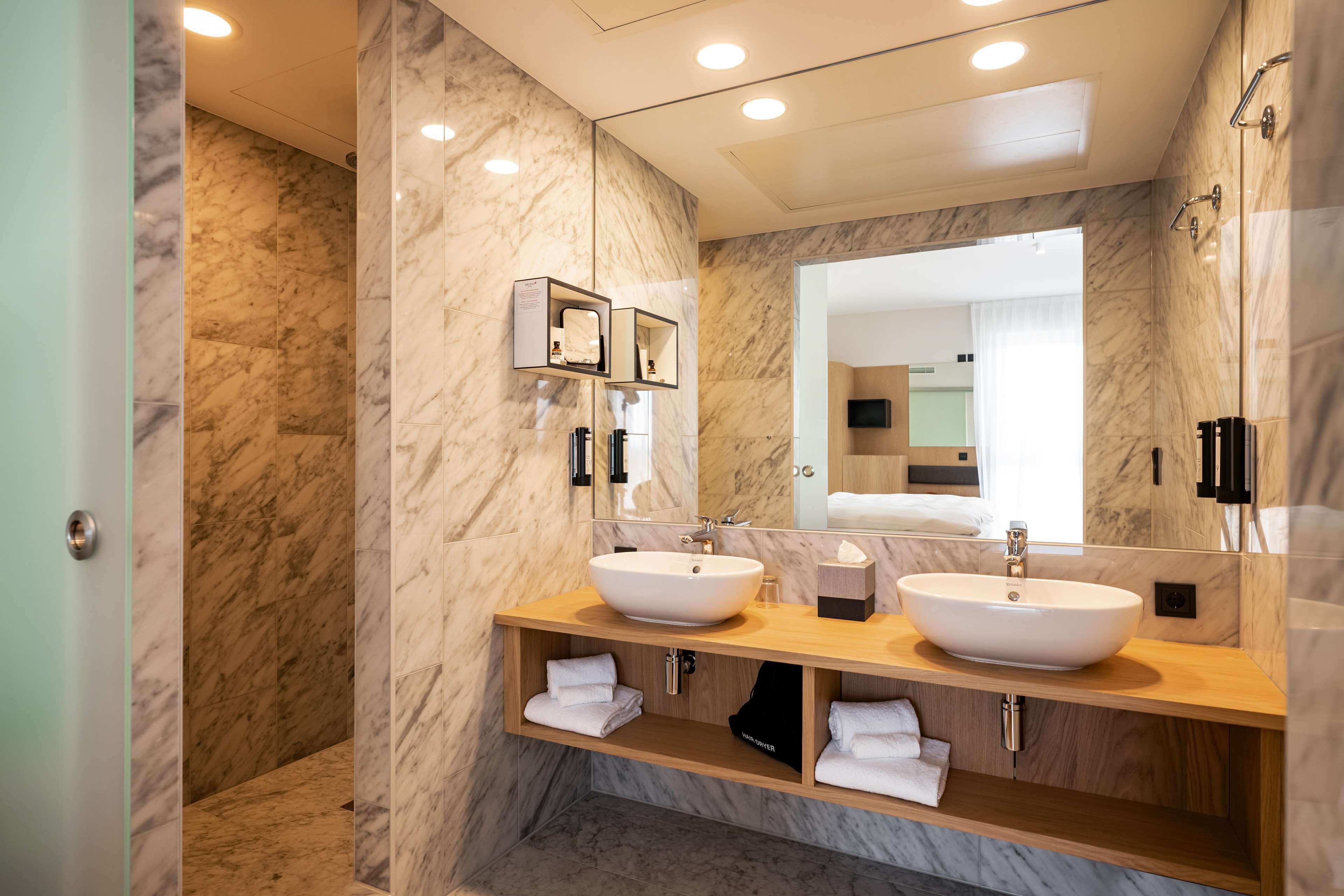 A modern bathroom with two sinks, marble walls, and a large mirror.