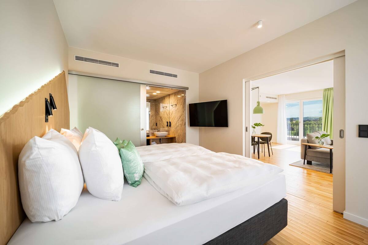 Une chambre moderne avec un grand lit, un téléviseur fixé au mur et une vue sur le balcon.
