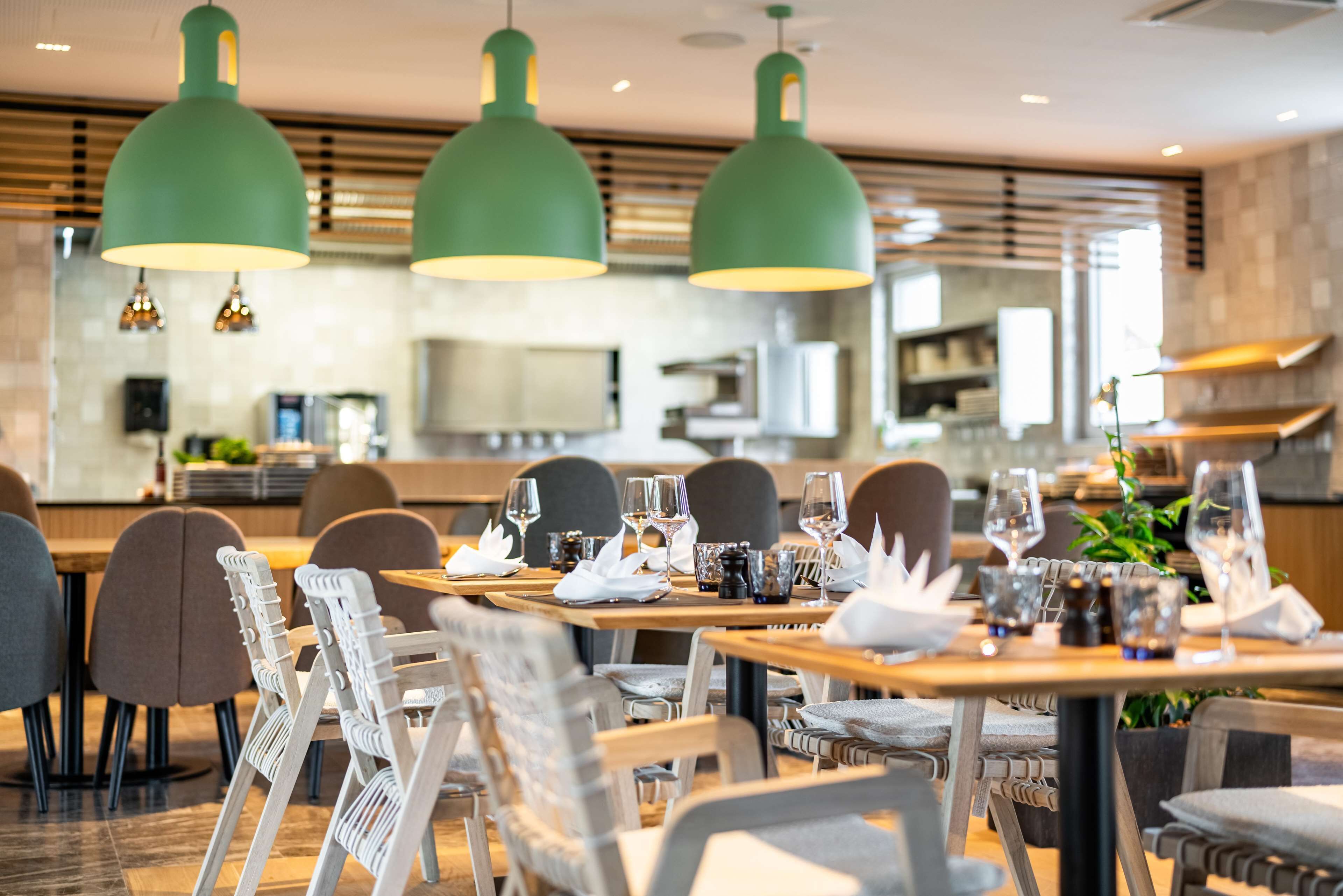 Um restaurante com mesas de madeira, cadeiras brancas e iluminação pendente verde.