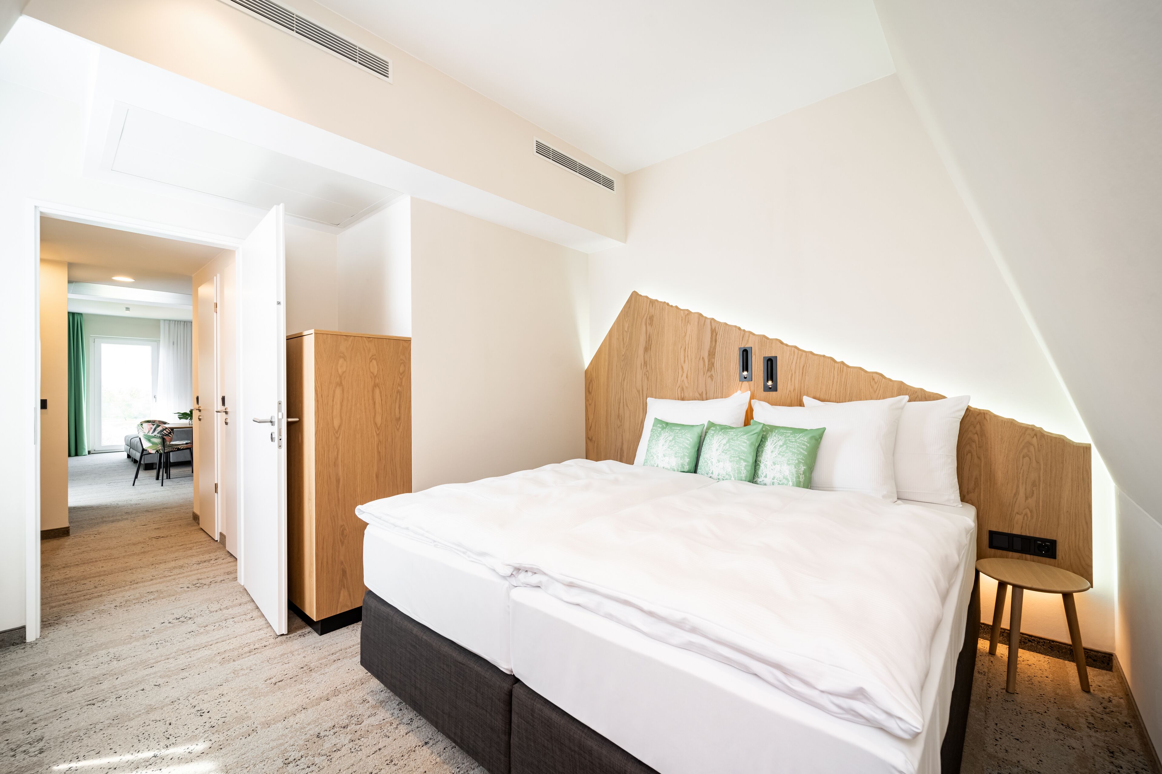 Ein modernes Hotelzimmer mit einem großen Bett, einem hölzernen Kopfteil und einem kleinen Nachttisch.