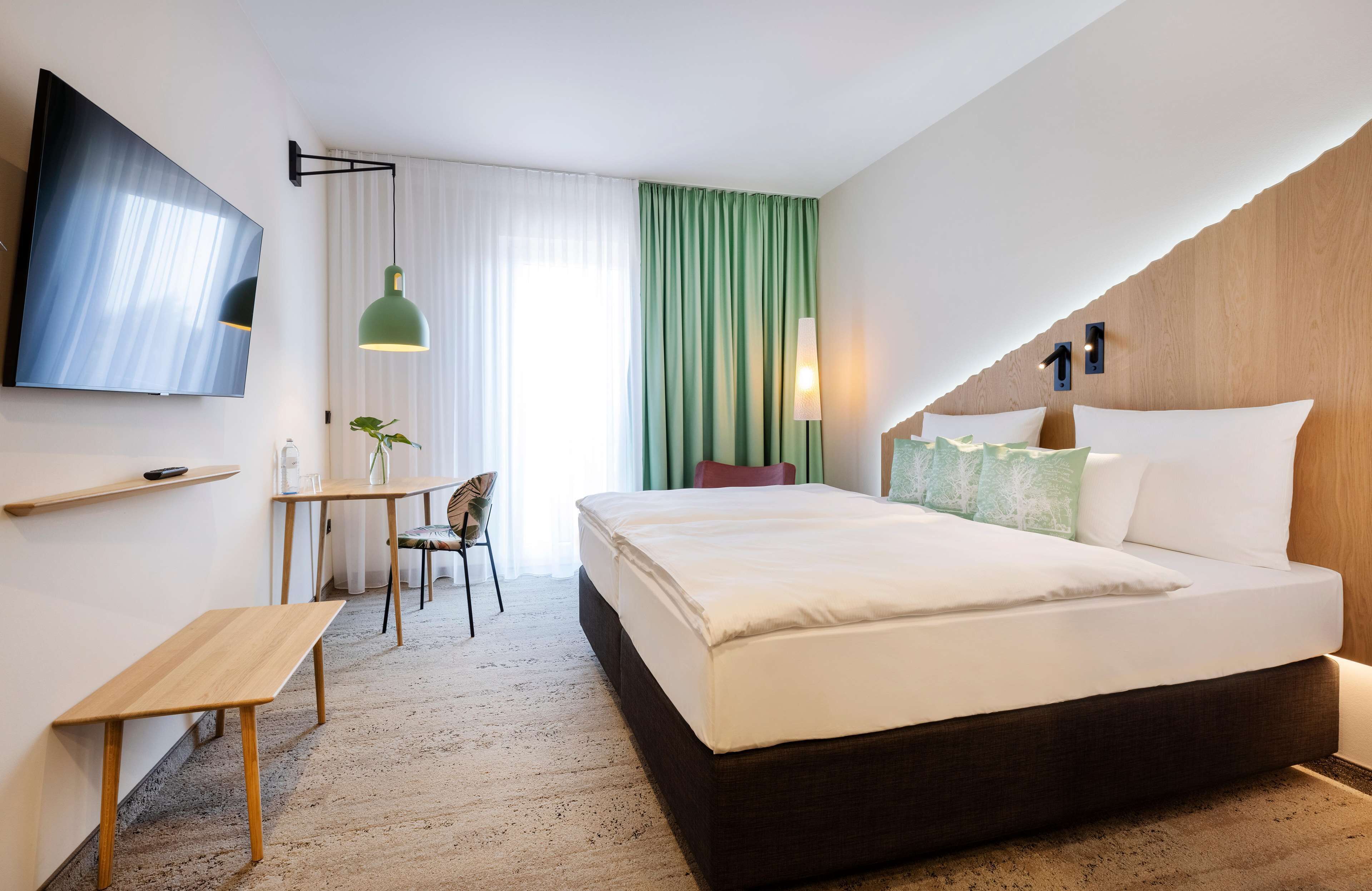 Habitación de hotel con cama, escritorio, silla, televisor y ventana con cortinas.