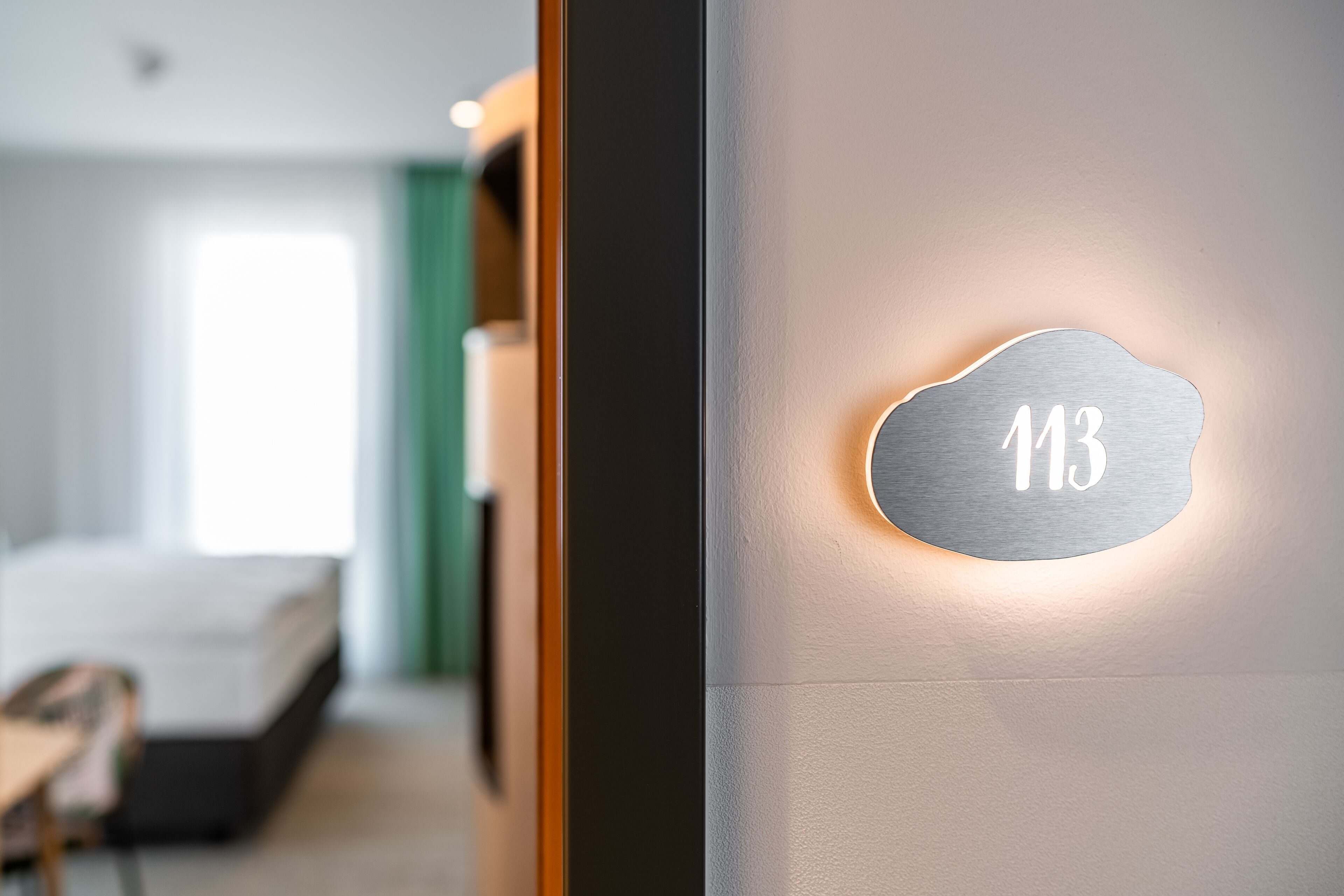 Ein modernes Hotelzimmer mit Bett, Schreibtisch und einer an der Wand befestigten Zimmernummer '113'.