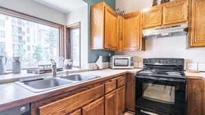 Una cocina moderna con armarios de madera, una estufa negra, un microondas y un ventanal con vistas a edificios.