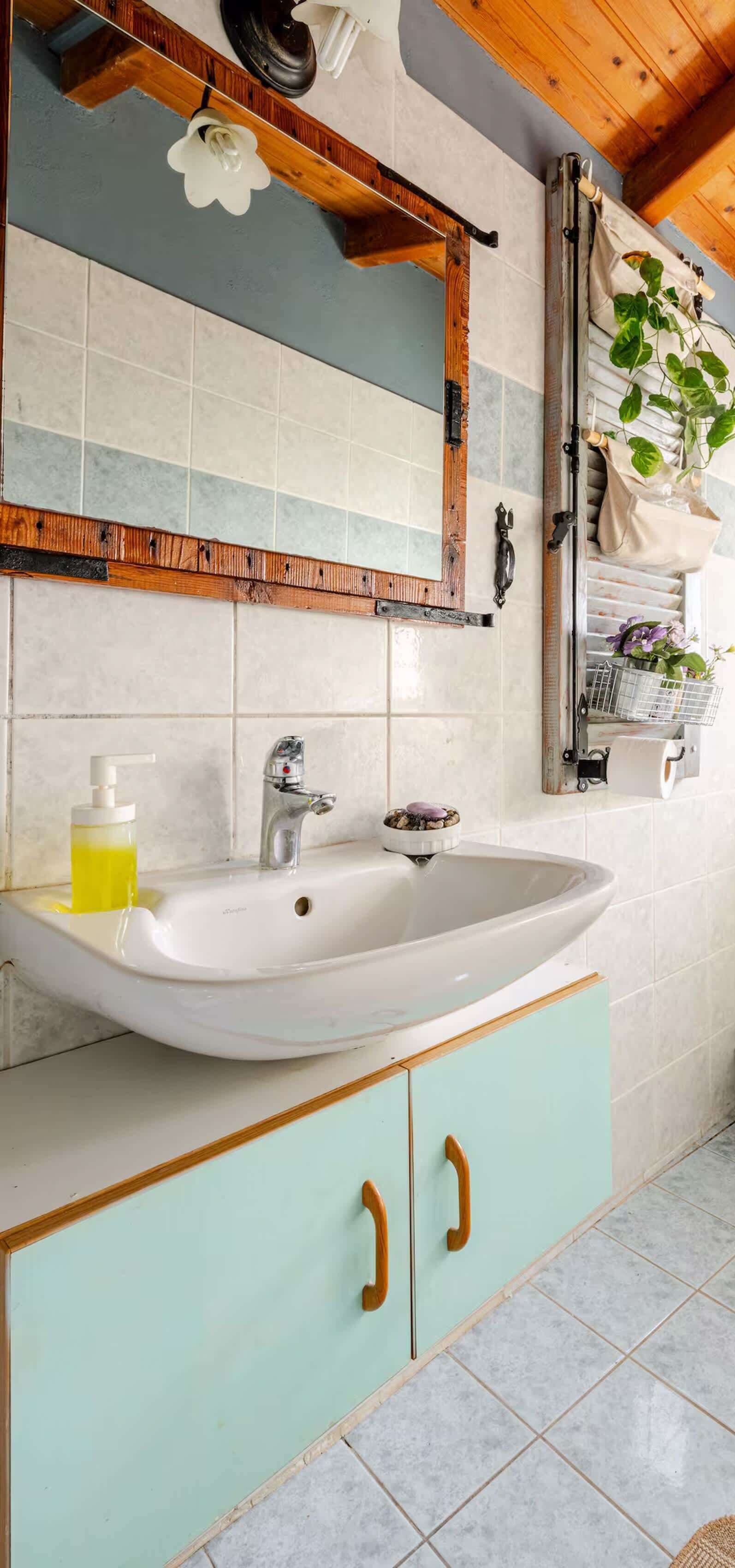A bathroom with a white sink, wooden cabinet, mirror, and tiled walls.