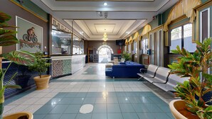 A hotel lobby with a reception desk, seating area, and decorative plants.