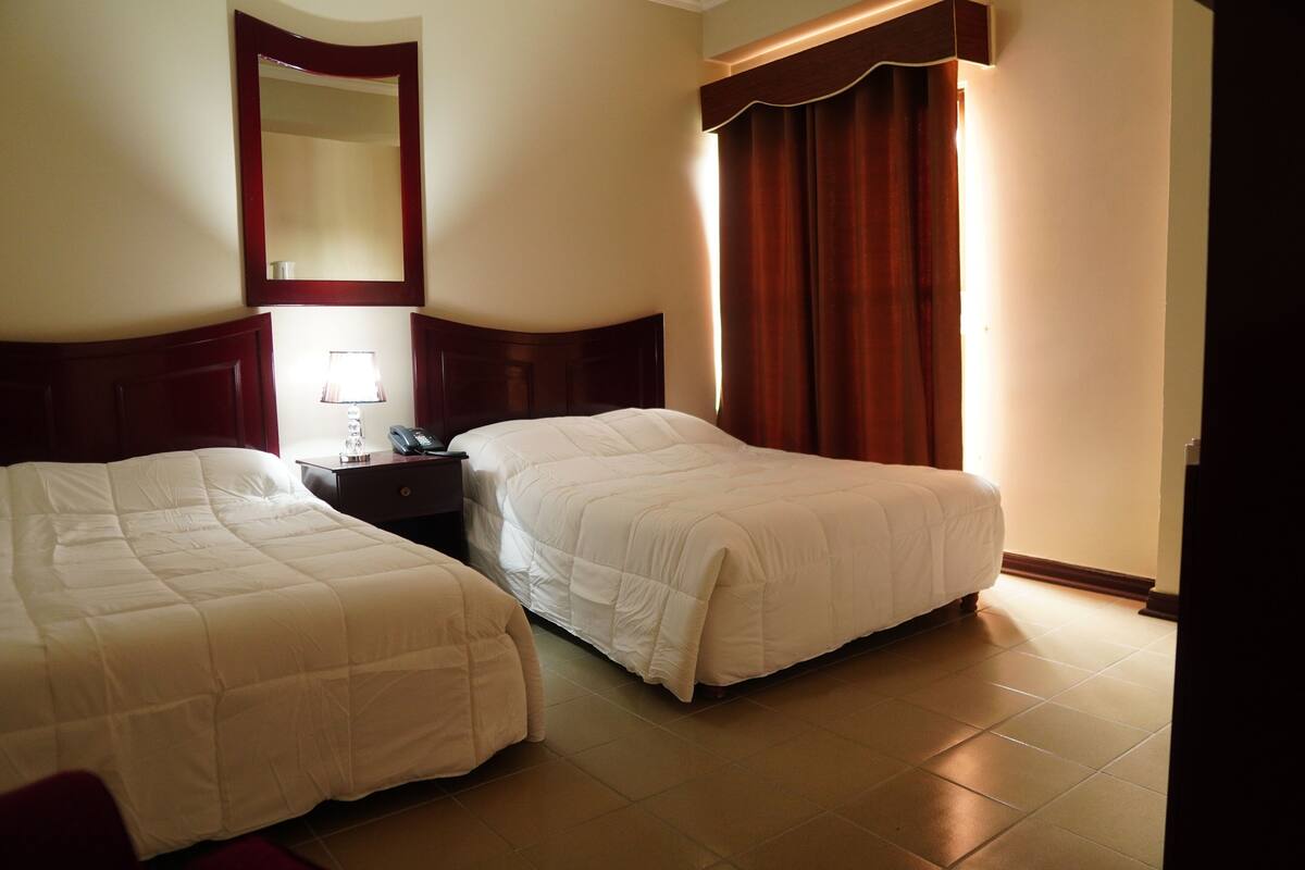 Une chambre d’hôtel avec deux lits, une table de chevet, une lampe et un grand miroir.