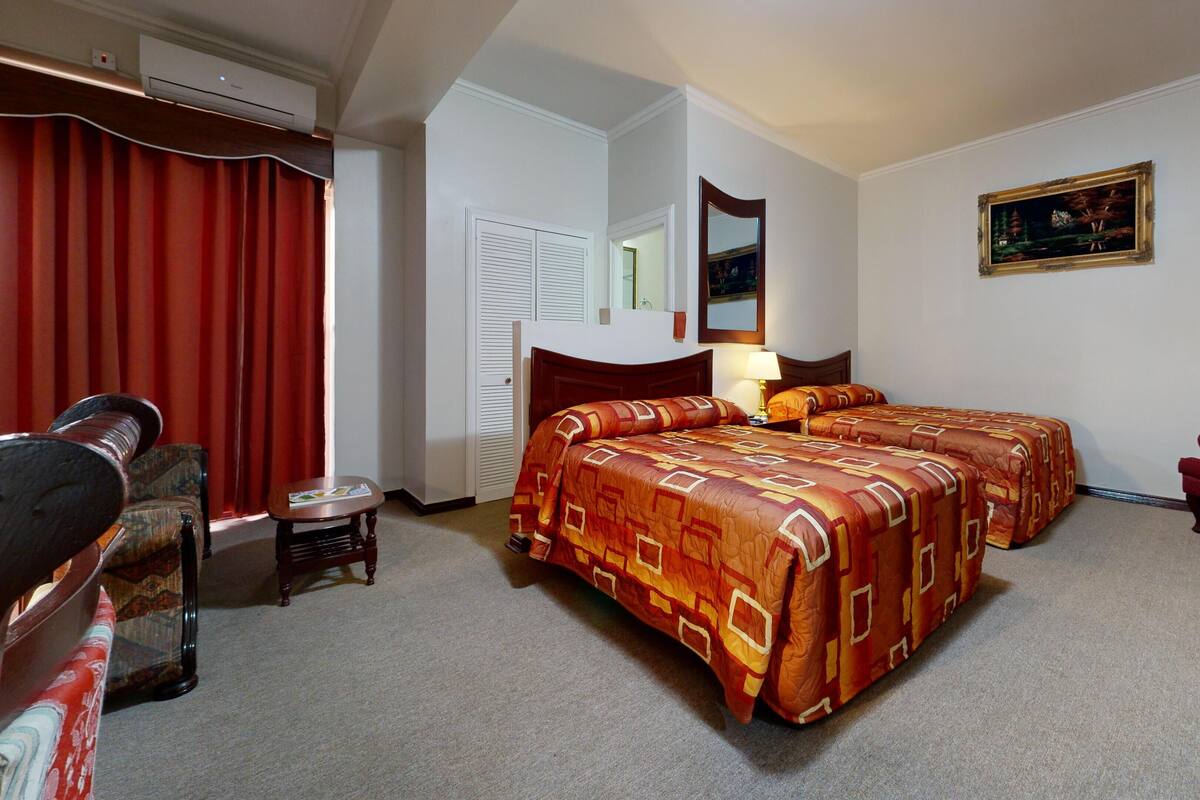 Une chambre d’hôtel avec deux lits, un bureau, une chaise, un miroir et un tableau au mur.