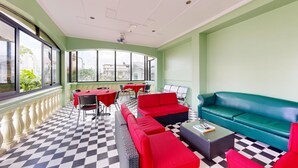 A sunlit indoor seating area with a checkered floor, red and teal sofas, and a table with chairs.