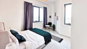 Ein modernes Schlafzimmer mit einem Bett, einem Sessel, einem kleinen Tisch und einem großen Fenster.