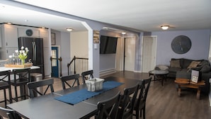 A spacious living area with a dining table, chairs, a sofa, and a TV mounted on the wall.