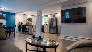 A modern kitchen with stainless steel appliances, a dining area with a glass table, and a living room with a large TV.