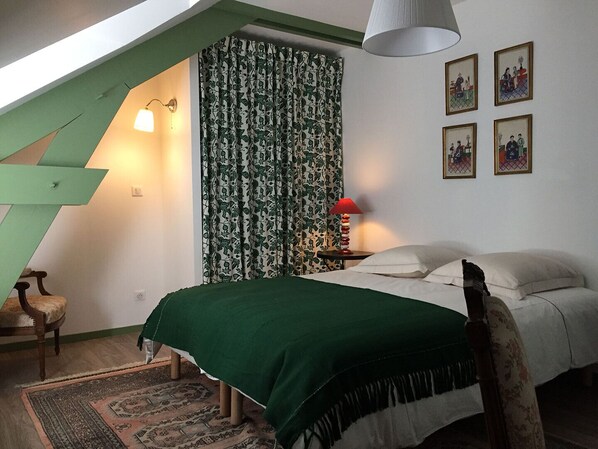 Une chambre à coucher avec une couvre-lit verte, un rideau à motifs, une lampe rouge et des tableaux encadrés accrochés au mur.