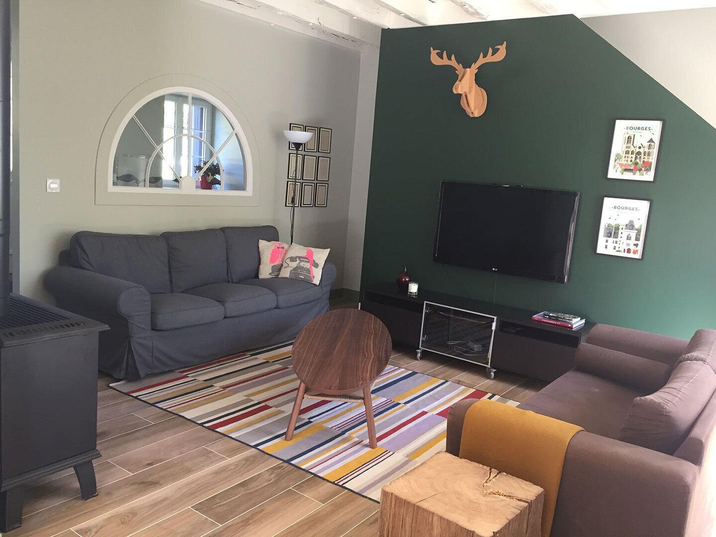 Un salon moderne avec un canapé gris, une table basse ronde en bois, un téléviseur fixé au mur et une tête de cerf décorative.