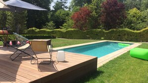 Una terraza de madera con piscina, sillas de descanso y un flotador hinchable verde.