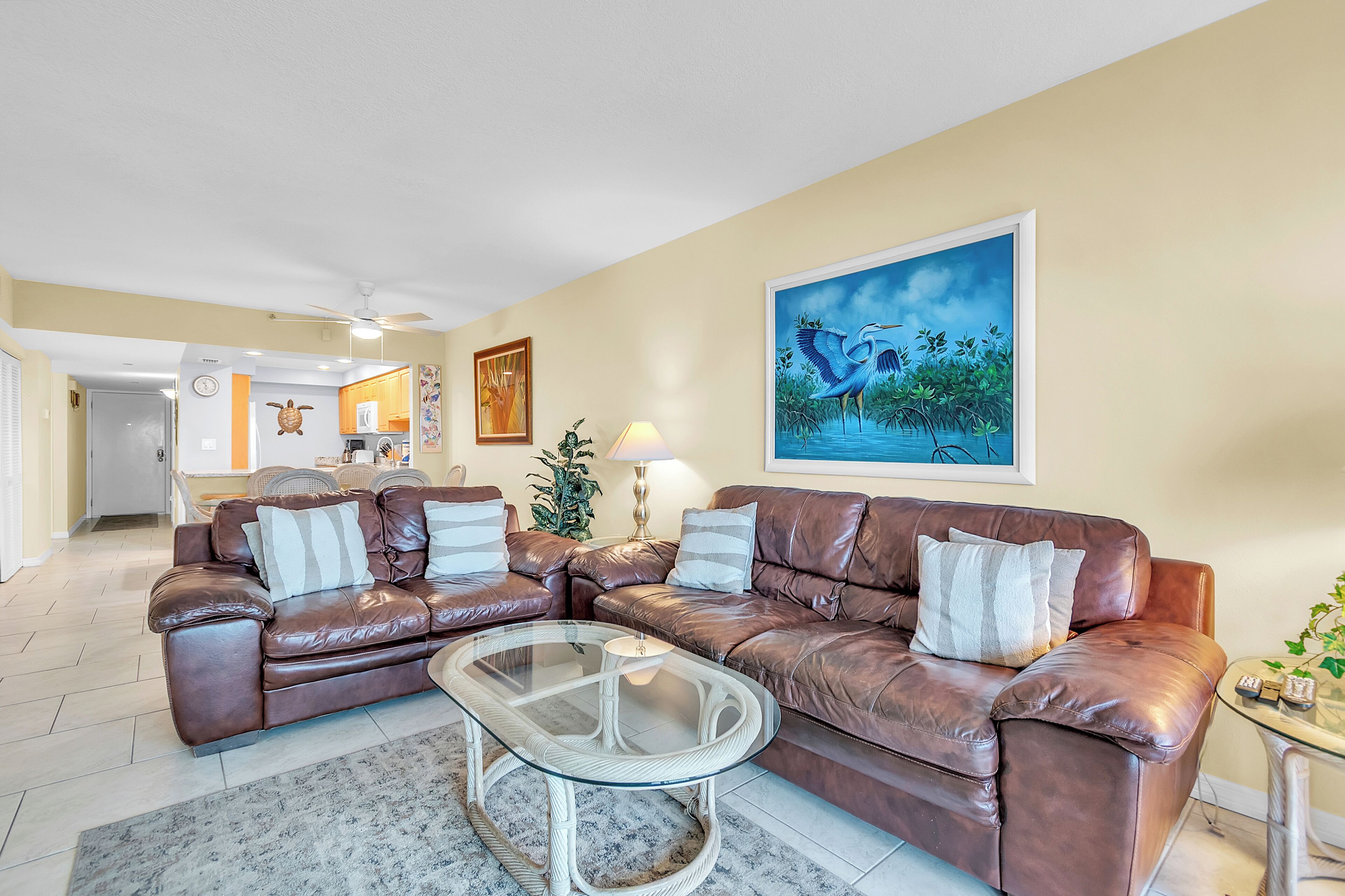 A living room with a brown leather sofa, a glass coffee table, and a painting of a bird.