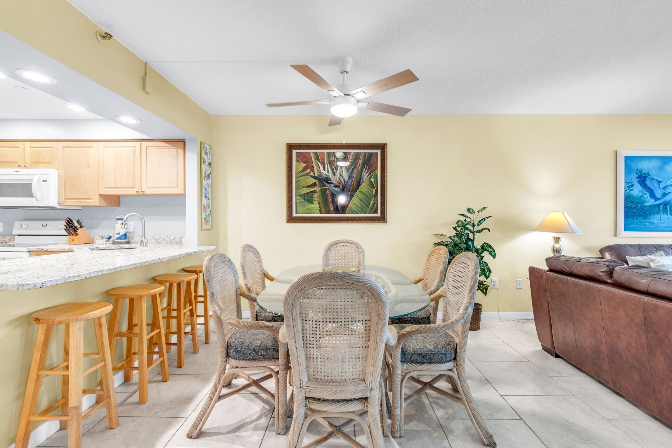 Un coin repas avec des chaises en osier, une table blanche et un ventilateur de plafond.