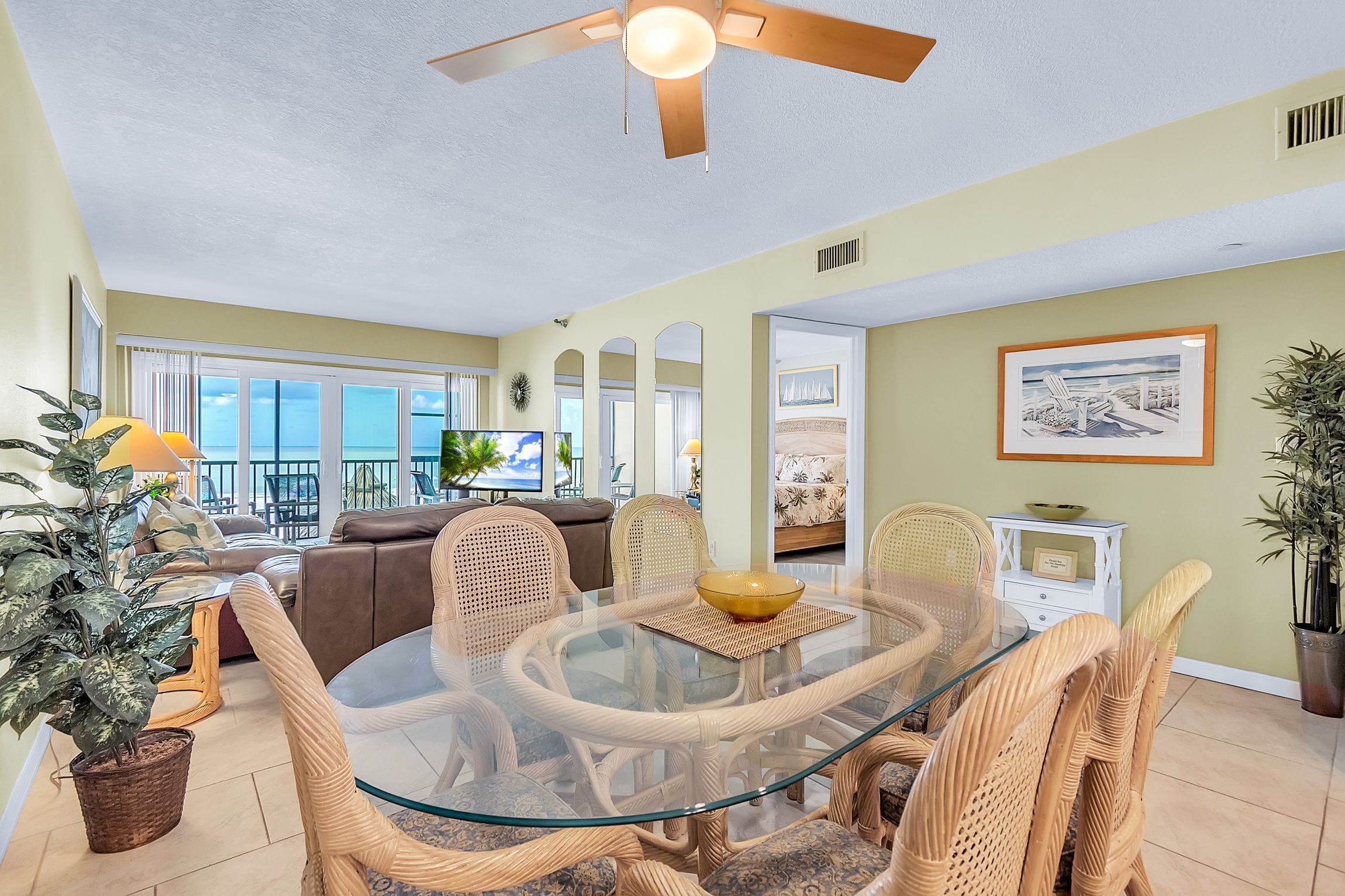 A dining area with a glass table, wicker chairs, and a ceiling fan.