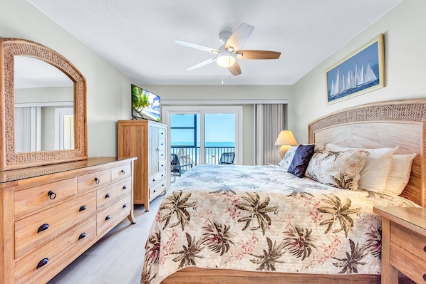 Ein Schlafzimmer mit Bett, Schminktisch, Deckenventilator und Blick auf den Balkon.