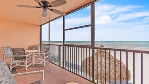A balcony with a ceiling fan, a table with chairs, and a view of the beach.