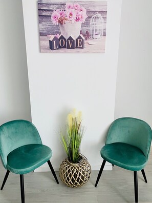 A room with two teal chairs, a decorative wall piece with flowers and the word 'LOVE,' and a woven plant pot.