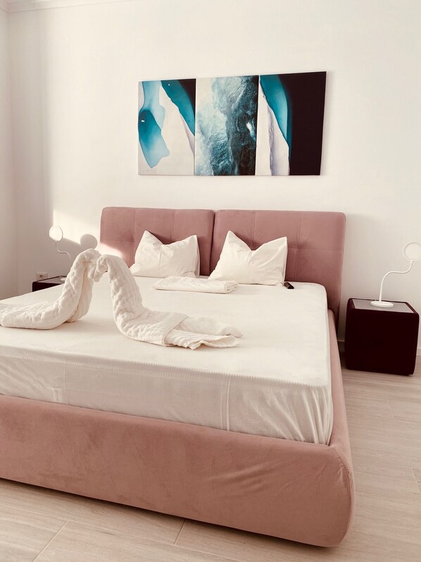 A modern bedroom with a large bed, a pink headboard, white bedding, and abstract wall art.