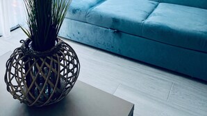 Uma sala de estar com um sofá azul, uma planta em vaso e uma obra de arte na parede.