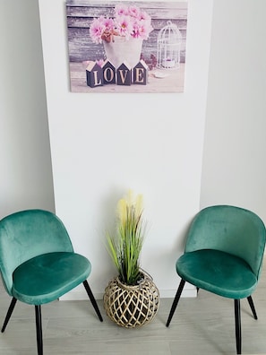 Une pièce comprenant deux fauteuils de couleur turquoise, un élément décoratif mural orné de fleurs et du mot « AMOUR », et un pot de fleurs en osier.
