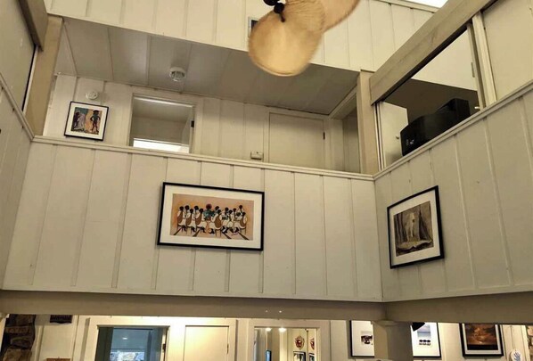 A multi-level interior with wooden paneling, framed artwork on the walls, and a ceiling fan.