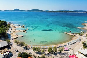 Une plage côtière aux eaux turquoise et limpides, bordée d’un rivage sablonneux et d’une rangée de parasols.