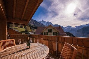 A wooden deck with a table and chairs, overlooking a mountain landscape. - Chalet Aquila 8 Penthouse (Lauterbrunnen)