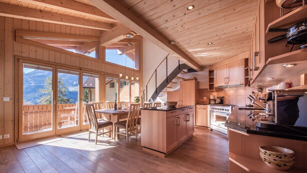 Un interior de madera con comedor, cocina y ventanas amplias con vistas a la montaña.