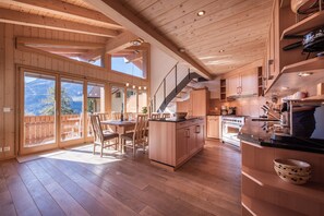 Interior em madeira com área de refeições, cozinha e janelas amplas com vista para a montanha.