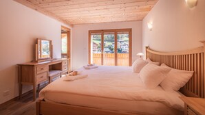 Un dormitorio con techo de madera, una cama con ropa blanca, un aparador de madera y una ventana con vistas a casas.